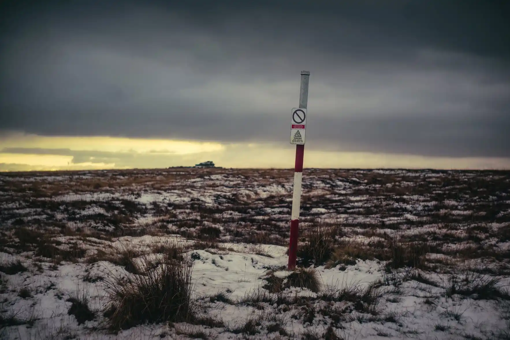Red-and-white range pole and warning notice on open Dartmoor moorland
